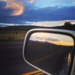 car's side mirror reflecting sunset in the mountains