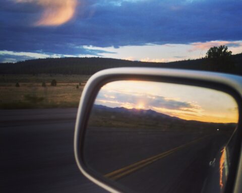 car's side mirror reflecting sunset in the mountains