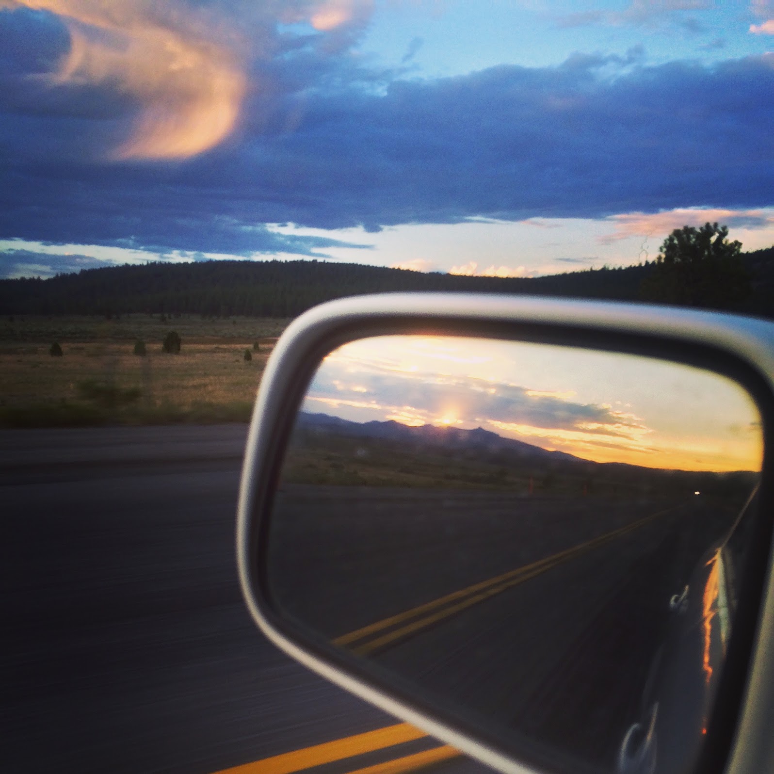 car's side mirror reflecting sunset in the mountains